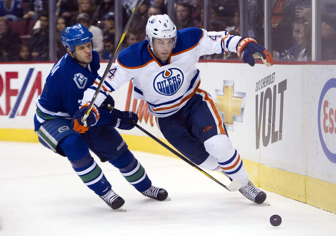 VANCOUVER, CANADA - DECEMBER 26: Kevin Bieksa #3 of the Vancouver Canucks knocks the puck away from Taylor Hall #4 of the Edmonton Oilers during the first period in NHL action on December 26, 2011 at Rogers Arena in Vancouver, British Columbia, Canada. (Photo by Rich Lam/Getty Images)