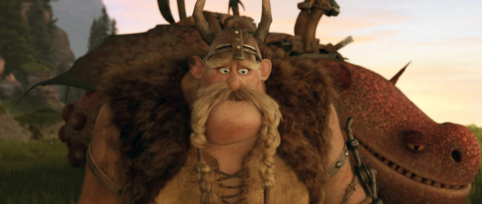 Animated character Gobber, from "How to Train Your Dragon," wears a Viking helmet and fur vest, standing in front of a dragon