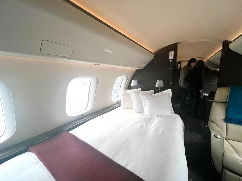 The double bed on board a VistaJet Bombardier Global 7500 with white sheets and a maroon blanket.