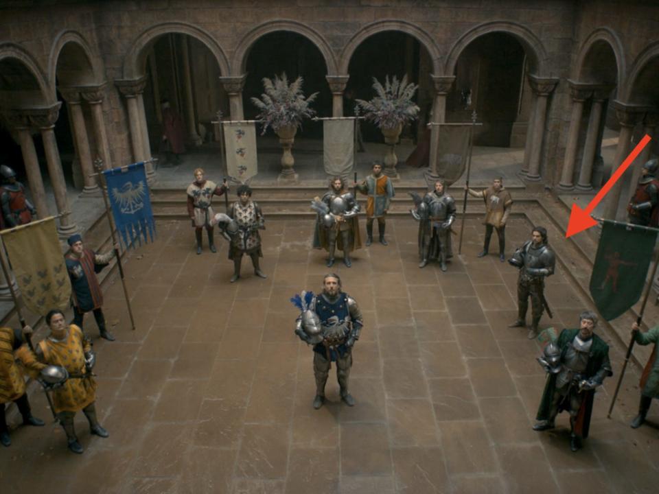 A group of men in varying colors of armor stand in a courtyard.