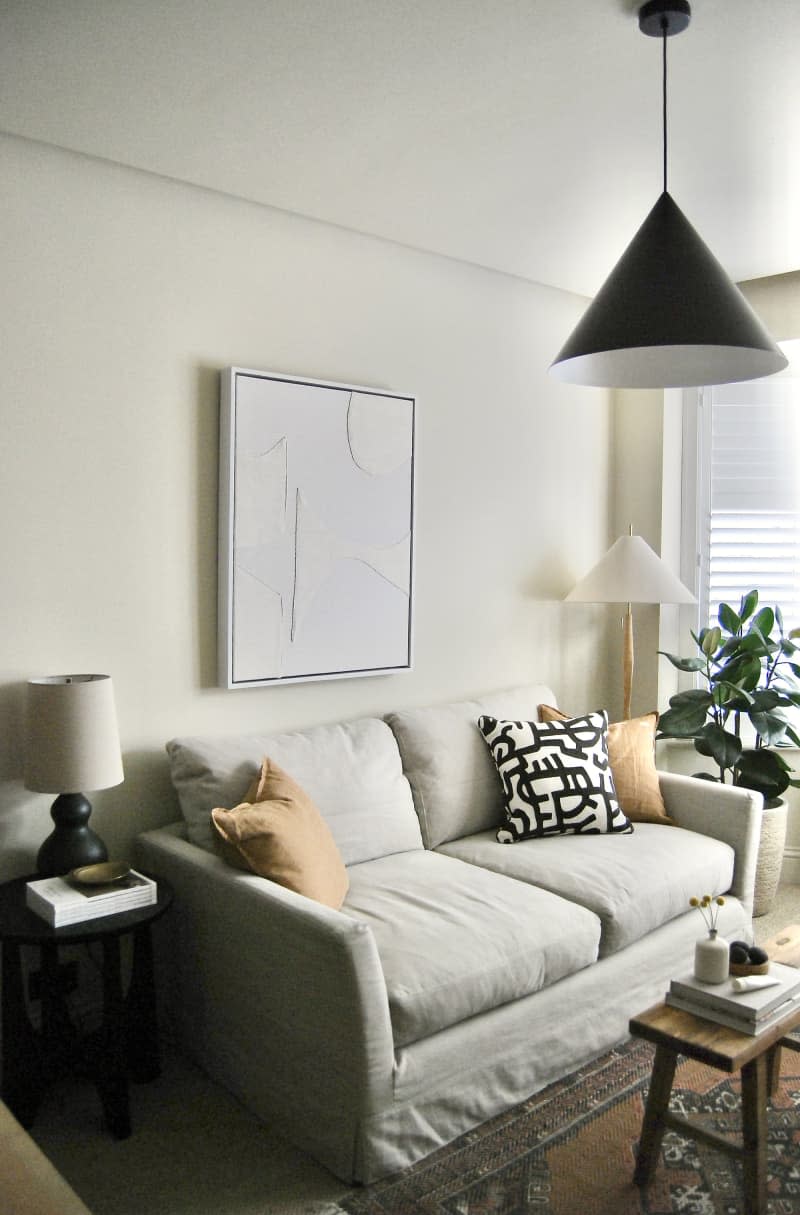 home office with pale gray sofa, lots of modern framed art, black pendant lamps, light wood furniture, natural rug with smaller patterned area rug