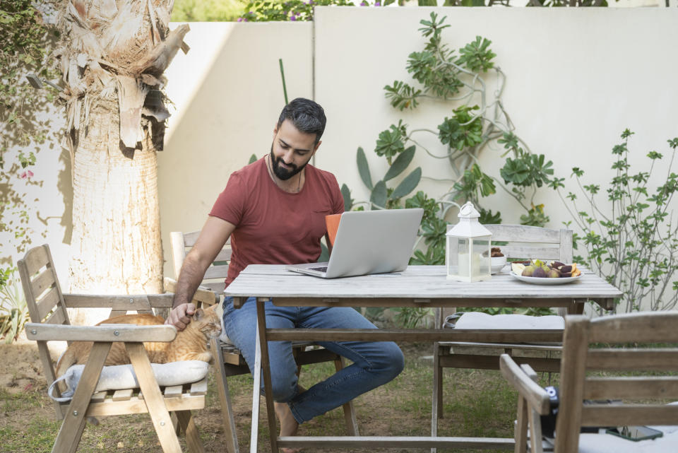 A man sitting in front of a laptop and petting his cat