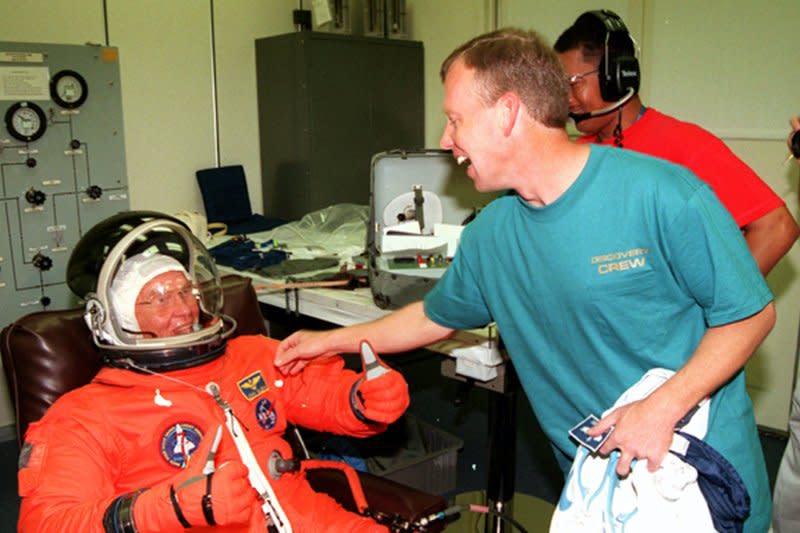 Pilot Steven W. Lindsey (R) reaches playfully for the name tag on the flight suit of Payload Specialist John H. Glenn Jr., on October 29, 1998. File Photo courtesy of NASA