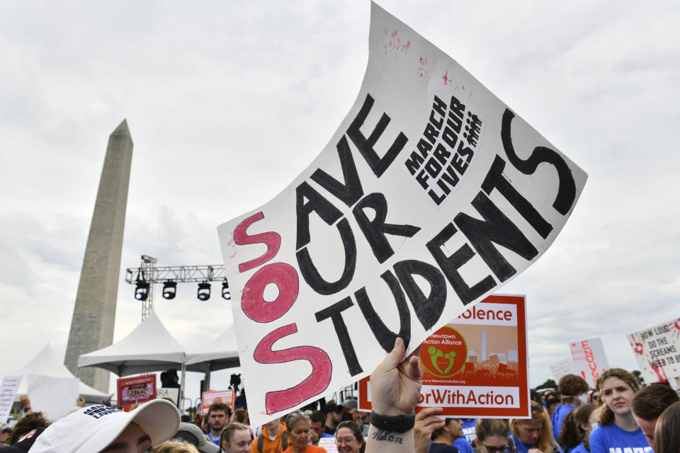 A sign reading Save Our Students is held in the air with the Washington Monument in the background.