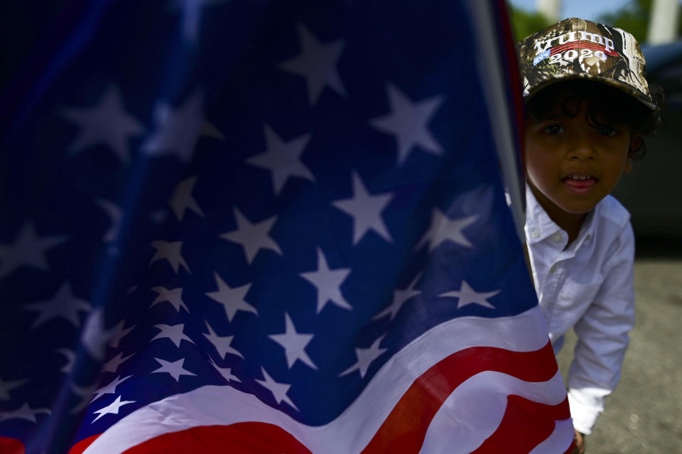 A boy carries the U.S. flag while wearing a pro-Trump cap moments before leaving for the headquarters of the Republican party in support of President Donald Trump's candidacy a few weeks before the presidential election next November, in Carolina, Puerto Rico, Sunday, Oct. 18, 2020. President Donald Trump and former Vice President Joe Biden are targeting Puerto Rico in a way never seen before to gather the attention of tens of thousands of potential voters in the battleground state of Florida. (AP Photo/Carlos Giusti)