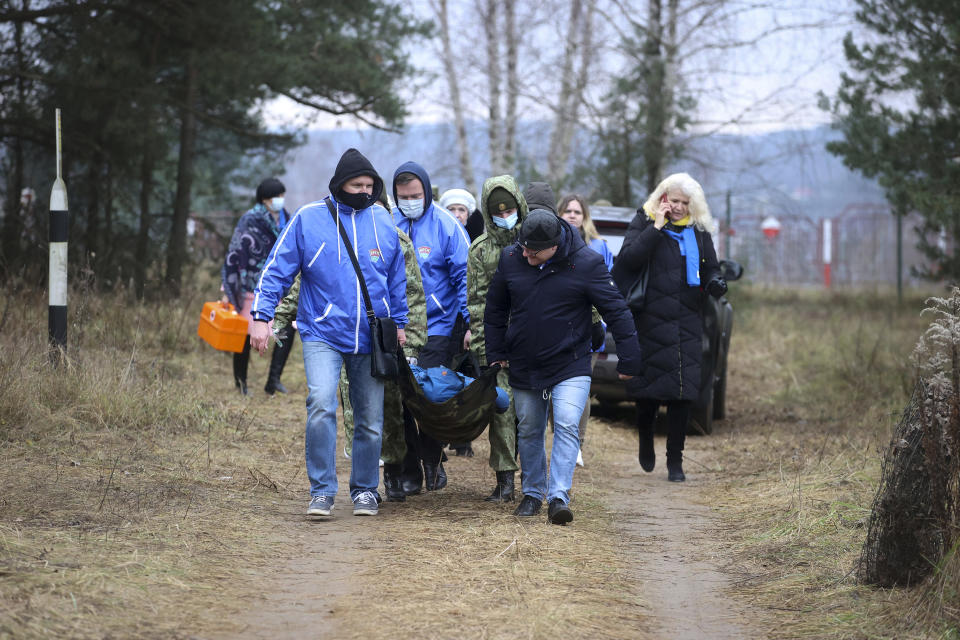 Belarusian volunteers carry a sick person as other migrants gather at the Belarus-Poland border near Grodno, Belarus, Saturday, Nov. 13, 2021. A large number of migrants are in a makeshift camp on the Belarusian side of the border in frigid conditions. Belarusian state news agency Belta reported that Lukashenko on Saturday ordered the military to set up tents at the border where food and other humanitarian aid can be gathered and distributed to the migrants. (Leonid Shcheglov/BelTA pool photo via AP)