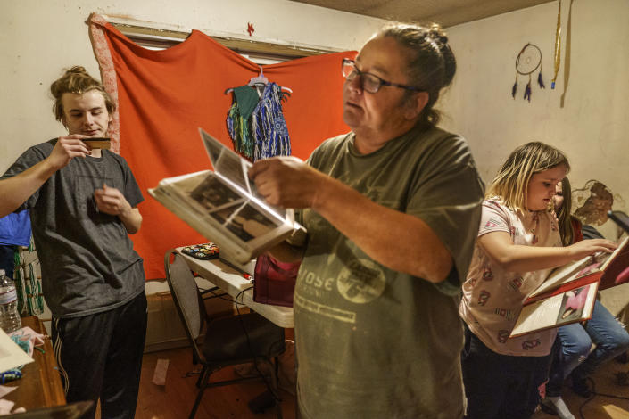 Betty Oppegard, center, whose daughter, Beth Renee Hill, died of an overdose involving methamphetamine, looks through family memorabilia with her grandchildren, Bruce, 16, left, and Robyn, 10, at her home in Naytahwaush, Minn., Thursday, Nov. 18, 2021. Oppegard used to wake up each morning and run through the names of her eight children from oldest to youngest, imagining where they were and what they were doing. She forced herself to stop, because when she got to Hill, if felt too much to bear. (AP Photo/David Goldman)