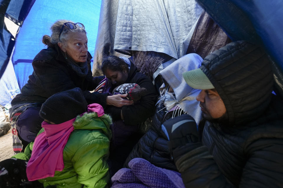 FILE - Medical volunteer Karen Parker, left, touches a 2-year-old child with a fever as she talks to a family of asylum-seeking migrants as they wait to be processed in a makeshift, mountainous campsite after crossing the border with Mexico, Feb. 2, 2024, near Jacumba Hot Springs, Calif. A federal judge on Friday, March 29, sharply questioned the Biden administration's position that it bears no responsibility for housing and feeding migrant children while they wait in makeshift camps along the U.S-Mexico border. (AP Photo/Gregory Bull, File)