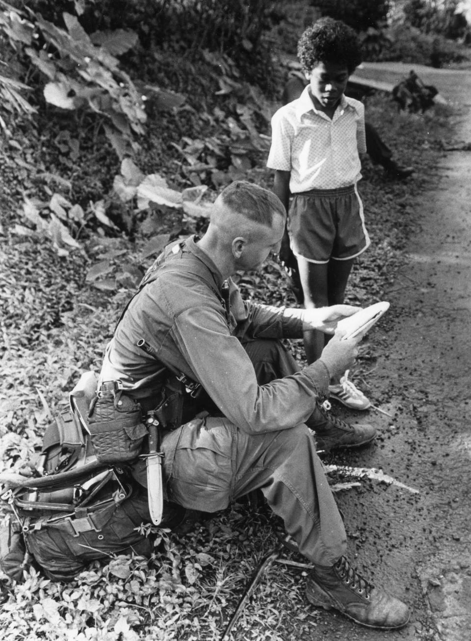 Staff Sgt. Dennis Tuggle of B Company, 2nd Battalion, 505th Parachute Infantry Regiment asks a kid for information in the Grenada highlands in November 1983.