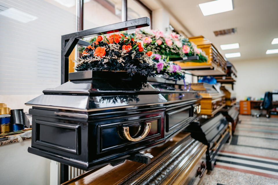 A funeral home's display area featuring various casket styles, with flower arrangements placed on top, likely meant for different choices of caskets