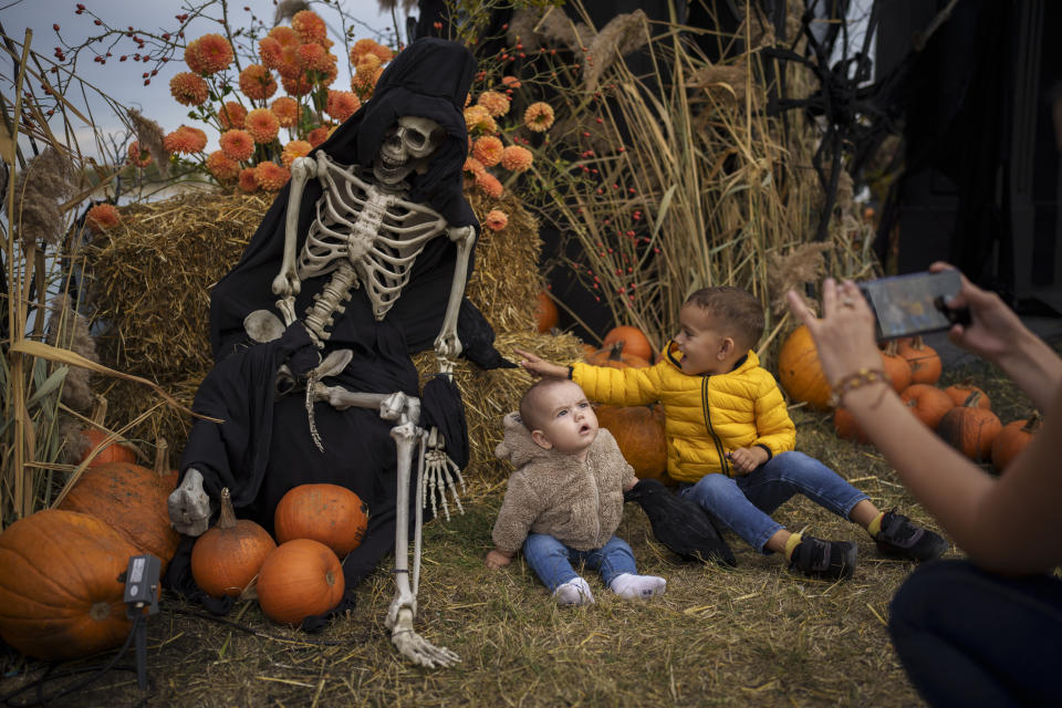 A woman takes photos of children next to decorations on the entrance path to the West Side Hallo Fest, a Halloween festival in Bucharest, Romania, Friday, Oct. 27, 2023. Tens of thousands streamed last weekend to Bucharest's Angels' Island peninsula for what was the biggest Halloween festival in the Eastern European nation since the fall of Communism. (AP Photo/Vadim Ghirda)