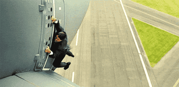 Tom Cruise hanging onto the side of an airplane during takeoff, performing a stunt scene