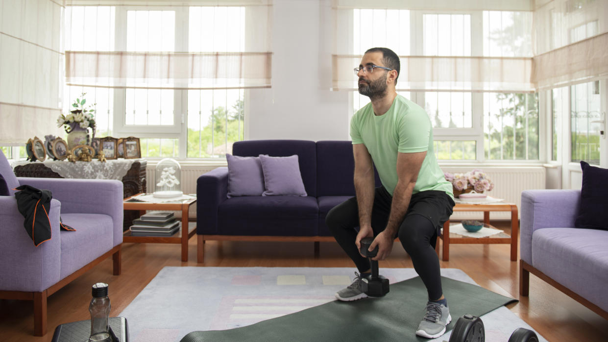  Man exercising with dumbbells at home in living room. 