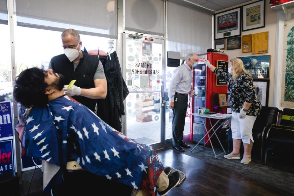 A stylist wearing a protective mask cuts a customer’s hair while another customer has their temperate checked at a barbershop in Atlanta, Georgia, on Monday.