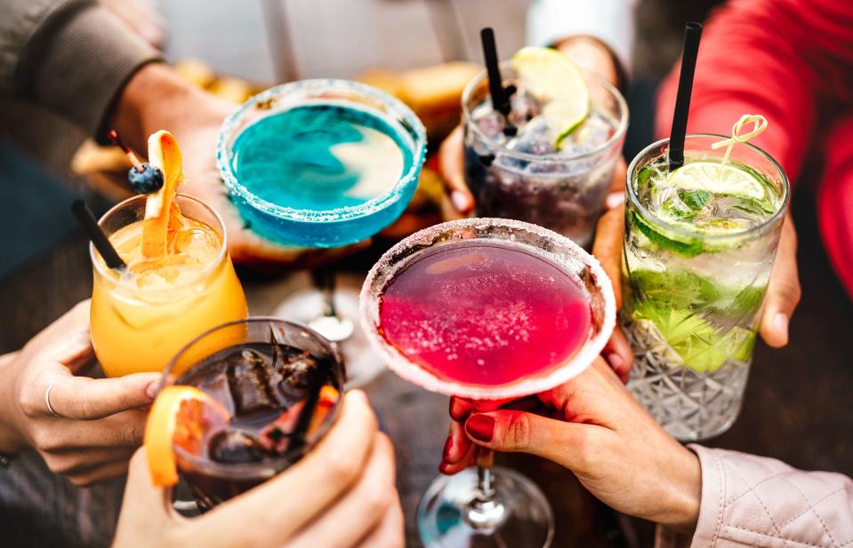 People hands toasting multicolored fancy drinks.