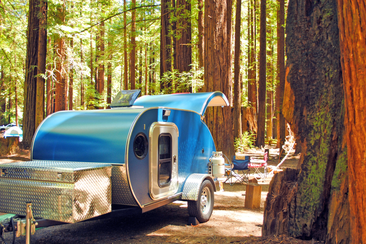 A blue teardrop camping trailer is setup at a campsite surrounded by redwood trees in Humboldt Redwoods State Park in California