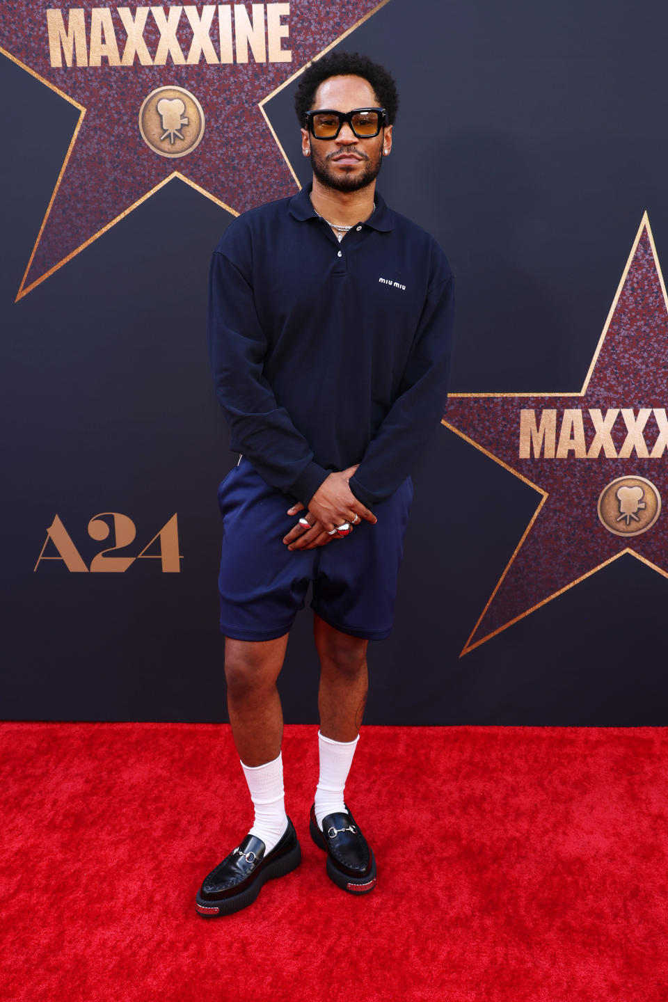 Kaytranada standing on the red carpet wearing a dark long-sleeve shirt, shorts, and loafers with socks