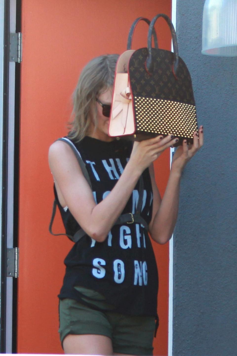 Taylor holding a Louis Vuiton bag in front of her face