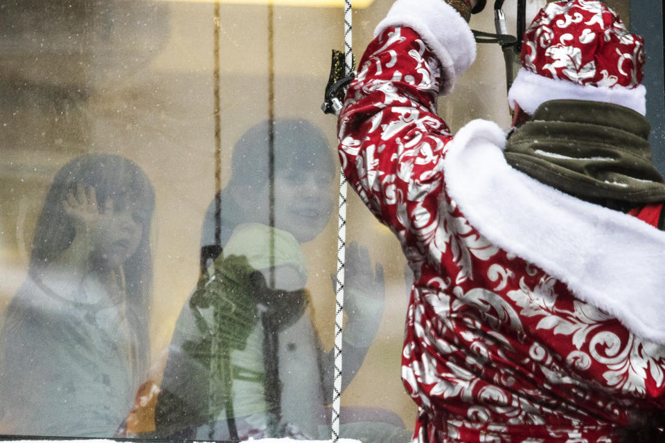 A Russian emergency rescue worker dressed as Ded Moroz (Santa Claus, or Father Frost) greets children as he scales the wall of a children hospital to mark the upcoming New Year celebrations, Russia, Friday, Dec. 25, 2020. Russia, which has so far registered more than 2.9 million confirmed cases of the virus and over 52,000 deaths in the pandemic, has been swept by a rapid resurgence of the outbreak this fall, with numbers of infections and deaths significantly exceeding those reported in the spring. Usually, performers come into children's rooms, but this year because of the virus-related restrictions, the artists had to perform outside of the hospital at a significant distance. (AP Photo/Pavel Golovkin)