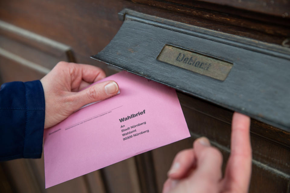 ILLUSTRATION - 26.03.2020, Bayern, Nürnberg: Eine Frau wirft ihre Briefwahlunterlagen für die Oberbürgermeister-Stichwahl am 29. März in Nürnberg in den Briefkasten des Wahlamtes. Am 29. März werden insgesamt in 750 Kommunen und Landkreisen die Ämter von Bürgermeistern, Oberbürgermeistern und Landräten per Stichwahl neu bestimmt. Foto: Daniel Karmann/dpa +++ dpa-Bildfunk +++