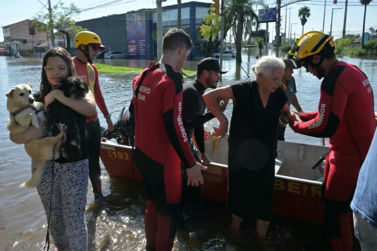 Bomberos y socorristas ayudan a Lorena a bajar del bote en el que fue rescatada junto a su hija, su yerno y su nieta de las inundaciones de Porto Alegre, el 6 de mayo de 2024 (NELSON ALMEIDA)