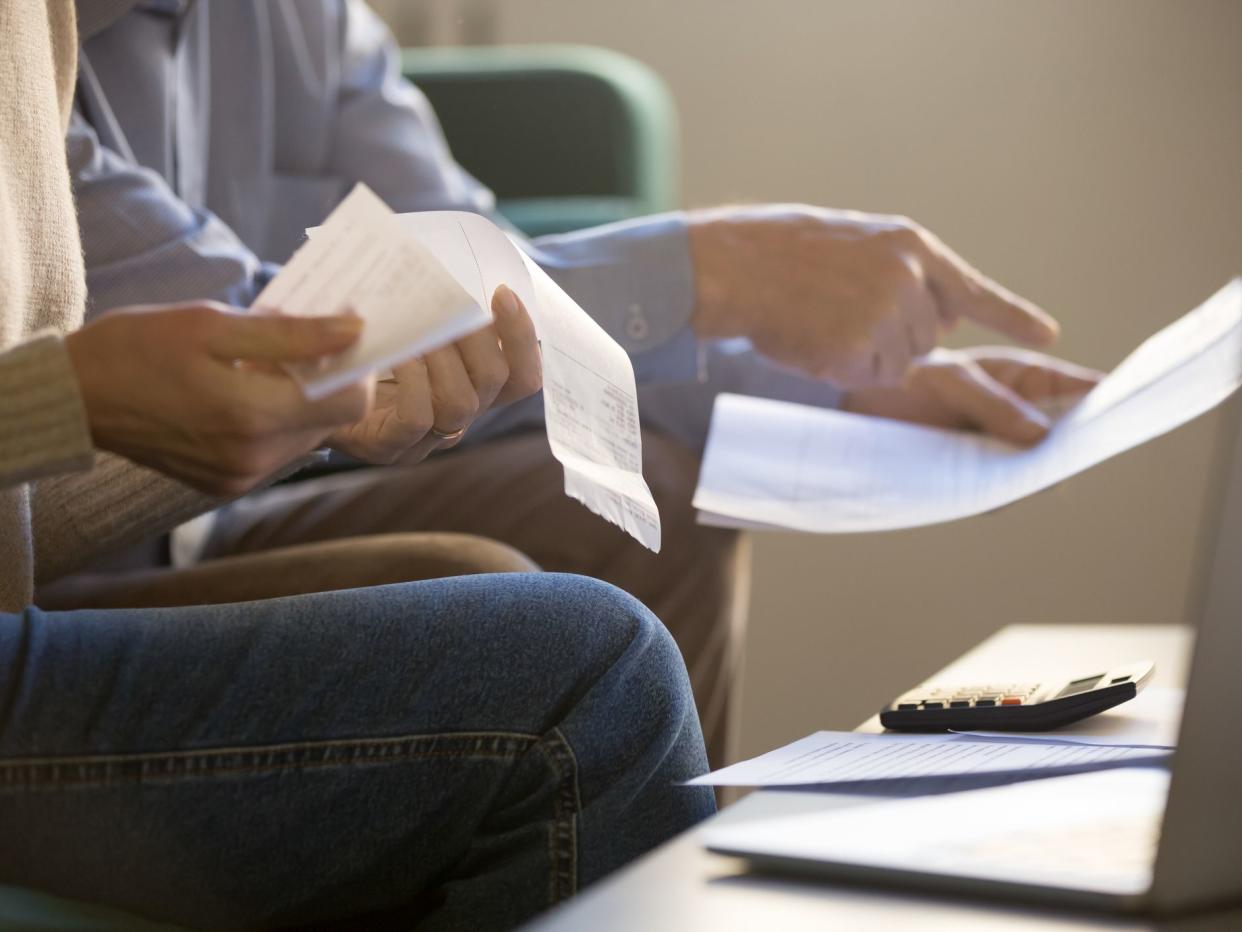 Elderly spouses sitting on couch at home planning budget check bills cheques, computer, documents and calculator on coffee table, close up cropped concept image, couple manage family expenses concept