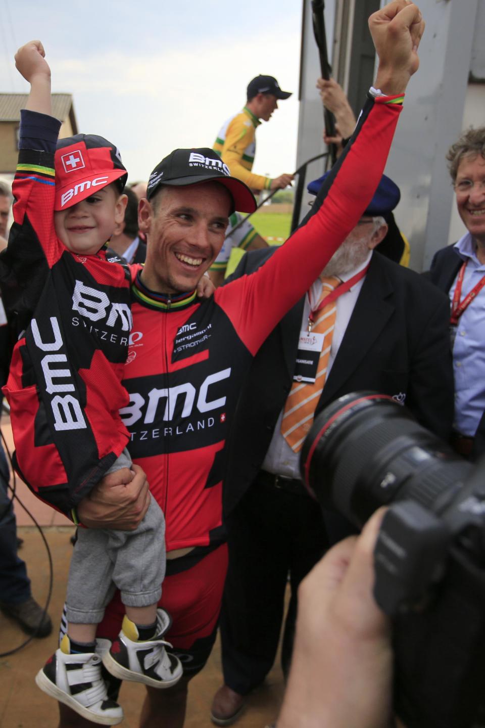 Belgium's Philippe Gilbert holds his three-and-a-half-year old son Alan as he celebrates winning the 49th edition of the Amstel Gold Cycling Race over 251.8 kilometers (156.5 miles) with start in Maastricht and finish in Valkenburg, southern Netherlands Sunday, April 20, 2014. Rear is third place Simon Gerrans of Australia who walks up to the podium.(AP Photo/Peter Dejong)