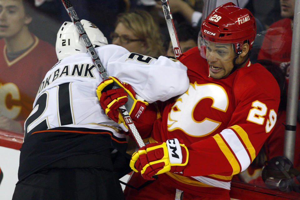 FILE - In this April 7, 2012, file photo, Anaheim Ducks' Sheldon Brookbank, left, checks Calgary Flames' Akim Aliu, a Nigerian-born Canadian, during third period NHL hockey action in Calgary, Alberta. Calgary Flames general manager Brad Treliving said the team is looking into an accusation that head coach Bill Peters directed racial slurs toward a Nigerian-born hockey player a decade ago in the minor leagues, then arranged for the player’s demotion when he complained. Akim Aliu tweeted Monday, Nov. 25, 2019, that Peters “dropped the N bomb several times towards me in the dressing room in my rookie year because he didn’t like my choice of music.” (AP Photo/The Canadian Press, Jeff McIntosh, File)