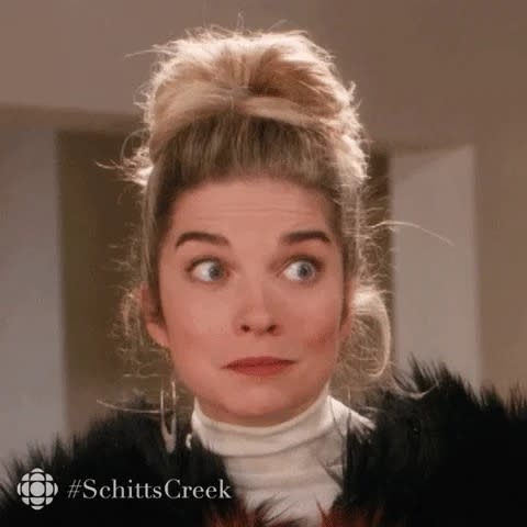 Annie Murphy in character with an updo hairstyle, wearing a black fur outfit, appearing surprised, with text "#SchittsCreek" and CBC logo on the bottom left