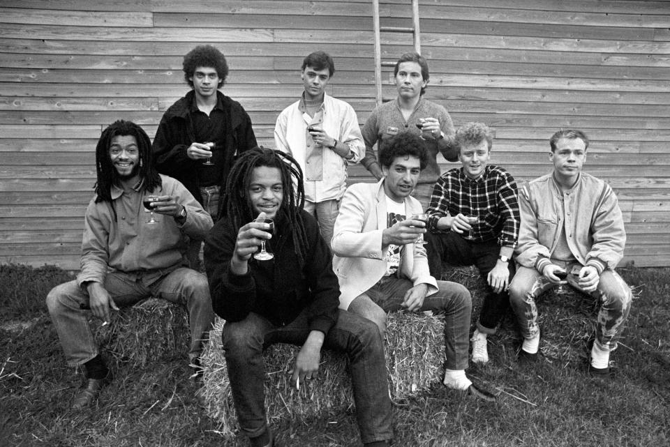 UB40 members sitting together on haystacks and holding wine glasses