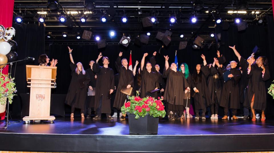 Students from CDC Vimont and CDC Lachute throw their graduation caps in the air to celebrate earning their high school diplomas, alongside Christina Shousha, director of the two adult education centres.