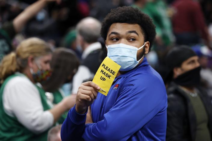 File - An usher at TD Garden holds a sign reminding people to wear a mask during the first half of an NBA basketball game between the Boston Celtics and the New York Knicks, Saturday, Dec. 18, 2021, in Boston. Workers and customers at restaurants, gyms and other indoor businesses in Boston will be required to show proof of coronavirus vaccination starting in mid-January in an effort to curb a rise in new cases across the city and state. An indoor mask mandate that takes effect Jan. 15, 2022, applies to restaurants, gyms, and indoor recreational facilities including theaters and sports venues, as well as some other businesses, according to Mayor Michelle Wu. (AP Photo/Mary Schwalm, File)