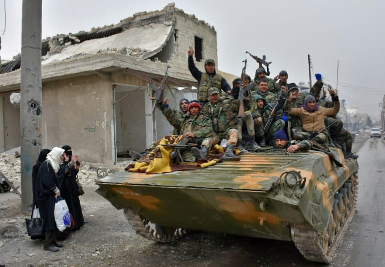 Syrian pro-government forces sit on a military vehicle driving past residents fleeing Aleppo in November 2016