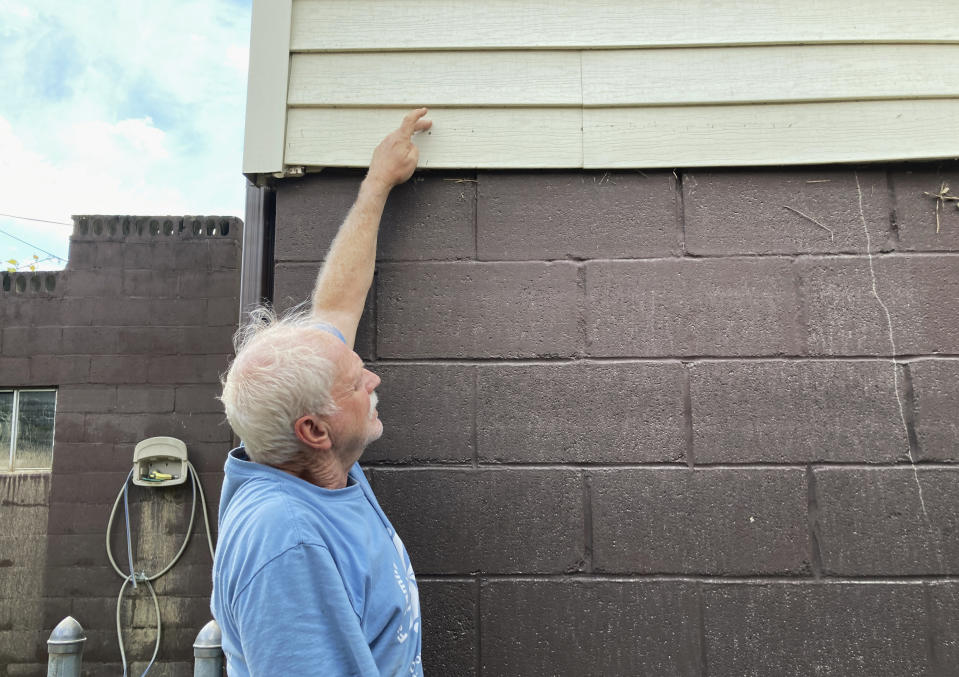 Paul Francis reaches to show how high floodwaters reached on the foundation of his house in Garrett, Ky., Saturday, July 30, 2022. He and his wife had to leave the house during the storms. Francis was born in the home 73 years ago but his wife wants to leave the area because of the flooding. (AP Photo/Dylan Lovan)