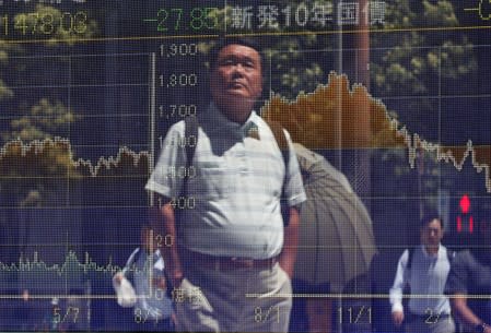 Passersby are reflected on a screen displaying graphs of market indices outside a brokerage in Tokyo