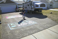 In this April 1, 2020, photo, Lisa Neuburger stands with her dog Bella by the camper she is living in and the chalk message she made in her former in-laws' driveway in St. Paul Park, Minn. Neuburger is living in the camper after being exposed to the coronavirus as an ICU nurse. (AP Photo/Jim Mone)