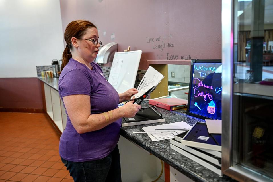 Jenniffer Reaser, owner of Delicious Delights Cakes, puts her food safety certificates in frames on Friday, Aug. 3, 2022, at her bakery at the Lansing Mall.