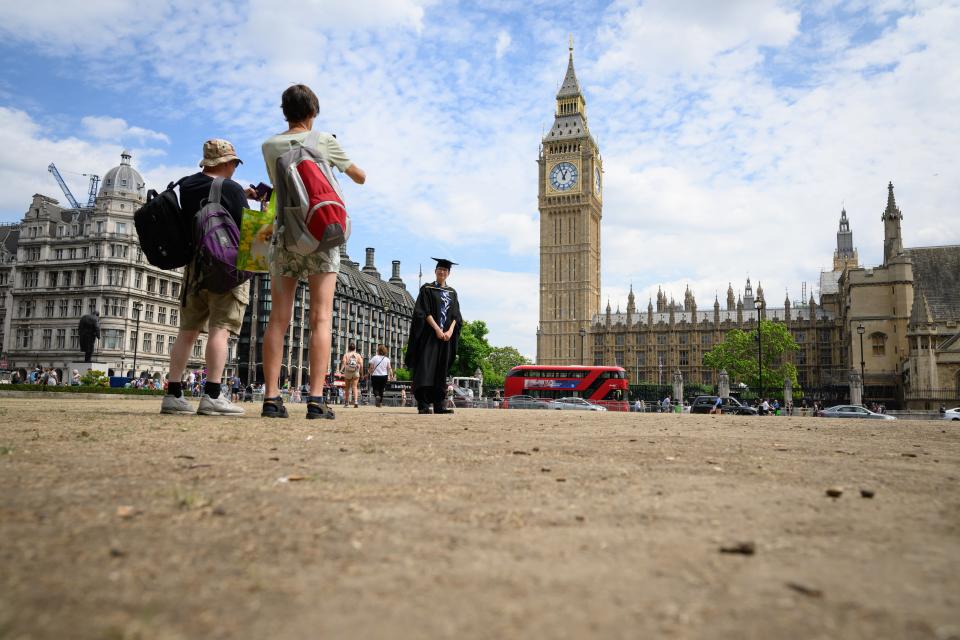 A university graduate poses for photos on the heat-scorched earth of Parliament Square on 13 July 2022 in London, England (Getty Images)