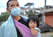 A man wearing a face mask walks with an infant on a sling in Imphal, India, Thursday, June 17, 2021. (AP Photo/Yirmiyan Arthur)