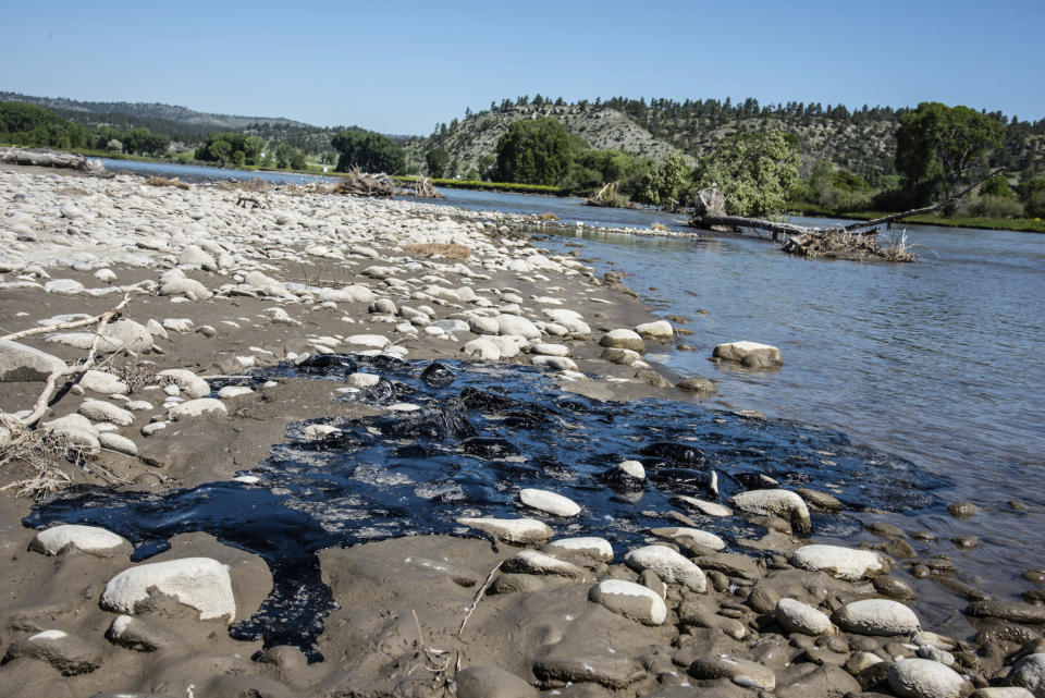 In this photo provided by Alexis Bonogofsky, petroleum products cover areas along the banks of the Yellowstone River near Columbus, Mont., July 1, 2023, following a freight train wreck last week in which tank cars fell into the river when a bridge collapsed. Officials with the Environmental Protection Agency said cleanup efforts began on Sunday, July 2, with workers cooling the asphalt binder with river water, rolling it up and putting the globs into garbage bags. (Alexis Bonogofsky via AP)