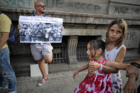 In this photo taken on Saturday, Sept. 19, 2020 kids play next to a man holding a banner showing children in a concentration camp and a paraphrase from a statement by Romanian President Klaus Iohannis that reads "Children get used to unpleasant things easily" during a protest against the COVID-19 pandemic restrictions in Bucharest, Romania. Across the Balkans and the rest of the nations in the southeastern corner of Europe, a vaccination campaign against the coronavirus is overshadowed by heated political debates or conspiracy theories that threaten to thwart the process. In countries like the Czech Republic, Serbia, Bosnia, Romania and Bulgaria, skeptics have ranged from former presidents to top athletes and doctors. Nations that once routinely went through mass inoculations under Communist leaders are deeply split over whether to take the vaccines at all. (AP Photo/Vadim Ghirda)