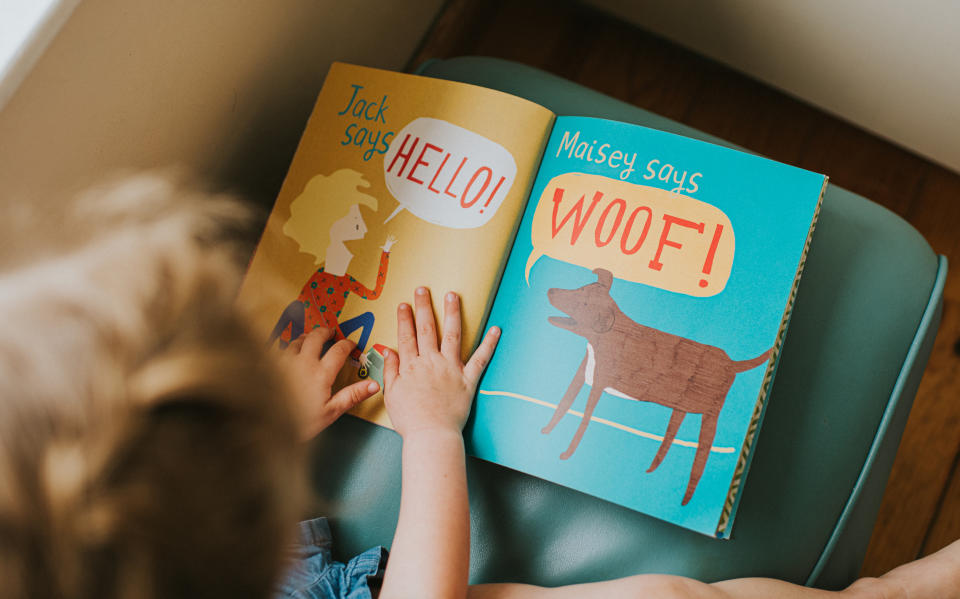 Child's hands turning page in a book with "HELLO!" and "WOOF!" text