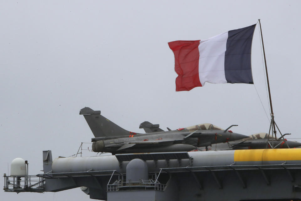 FILE - In this Friday, Feb. 21, 2020 file photo, a French flag flies near Rafale warplanes on the deck of the aircraft carrier Charles de Gaulle, docked at Cyprus' main port of Limassol. Greece's government says on Thursday, Dec. 17, 2020, it will pay 2.32 billion euros ($2.8 billion) for the purchase of French-made Rafale fighter jets and an upgrade of compatible air-to-air missile systems and part of a major military overhaul. (AP Photo/Petros Karadjias, File)