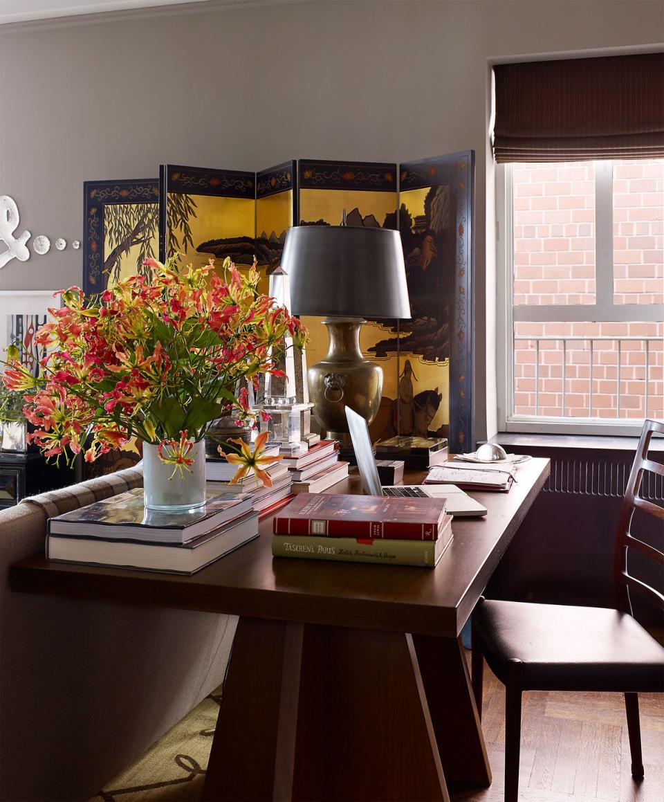 a dark wood triangle pedestal table with books and a lamp behind a sofa and a coromandel screen in the background