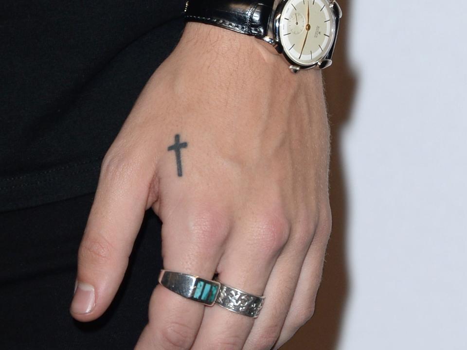 A small cross tattoo on Harry Styles' left hand.