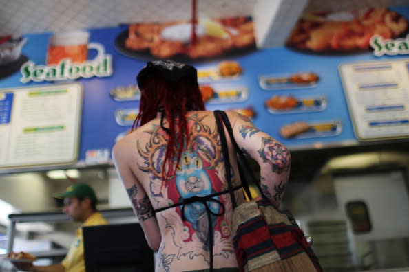 A woman with a series of tattoos on her back orders lunch at Nathan's at Coney Island on July 12, 2012 in the Brooklyn borough of New York City. Coney Island has until recently been viewed as a seedy and dilapidating seaside park, however, it is going through a gradual transition which many compare to the renovation of Times Square. In order to accommodate more shops and residential buildings, the Michael Bloomberg administration rezoned Coney Island in 2009. The city also bought seven acres of prime Coney Island real estate promising approximately $150 million in infrastructure upgrades in the area. A recent study found that Coney Island's Luna Park had 640,000 visitors in 2011, the most since Steeplechase Park closed in 1964. (Photo by Spencer Platt/Getty Images)