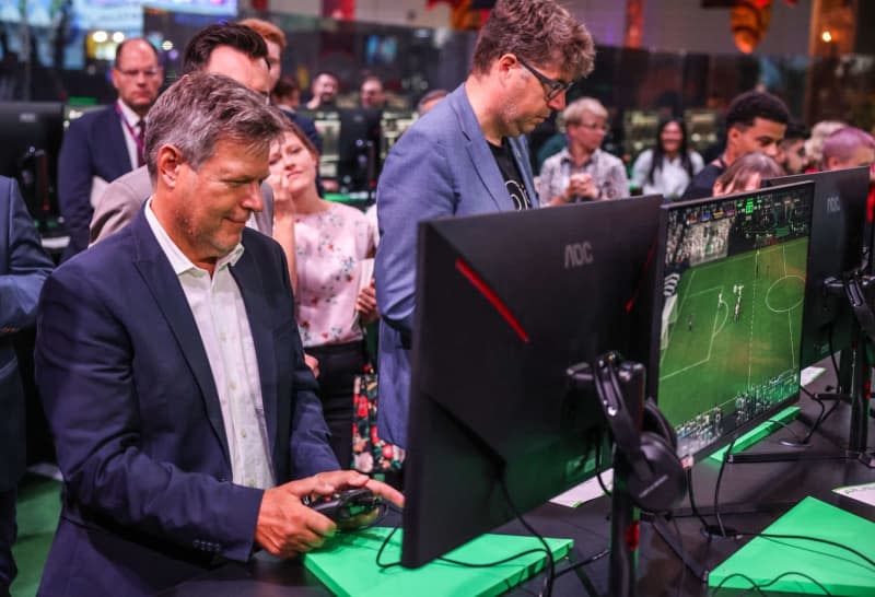 Robert Habeck (L), German Minister for Economic Affairs and Climate Protection, tests a computer game during his tour of Gamescom. The Gamescom computer and video games trade fair takes place in Cologne from August 21-25, 2024. Oliver Berg/dpa