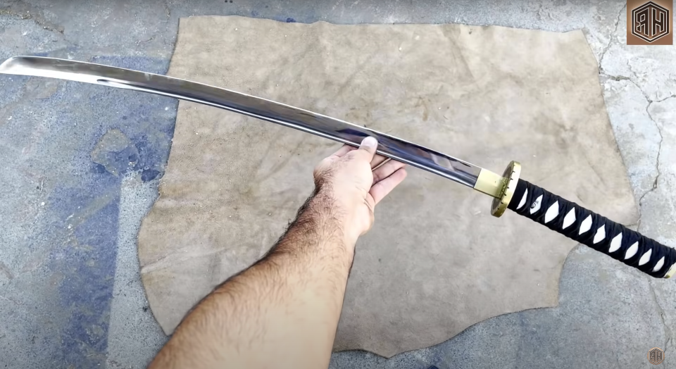 a photo of a man's hand holding a katana against a stone background