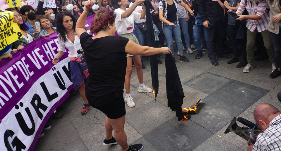 A woman burns her headscarf in protest of Amini's death in police custody in Iran.