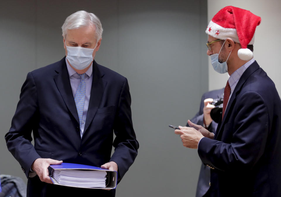 A collegue wears a Christmas hat as European Union chief negotiator Michel Barnier, left, carries a binder of the Brexit trade deal during a special meeting of Coreper, at the European Council building in Brussels, Friday, Dec. 25, 2020. European Union ambassadors convened on Christmas Day to start an assessment of the massive free-trade deal the EU struck with Britain. After the deal was announced on Thursday, EU nations already showed support for the outcome and it was expected that they would unanimously back the agreement, a prerequisite for its legal approval. (Olivier Hoslet, Pool via AP)